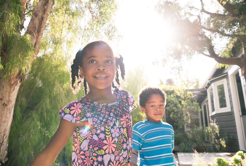 African American girl and boy hold hands and walk during a sunny day.