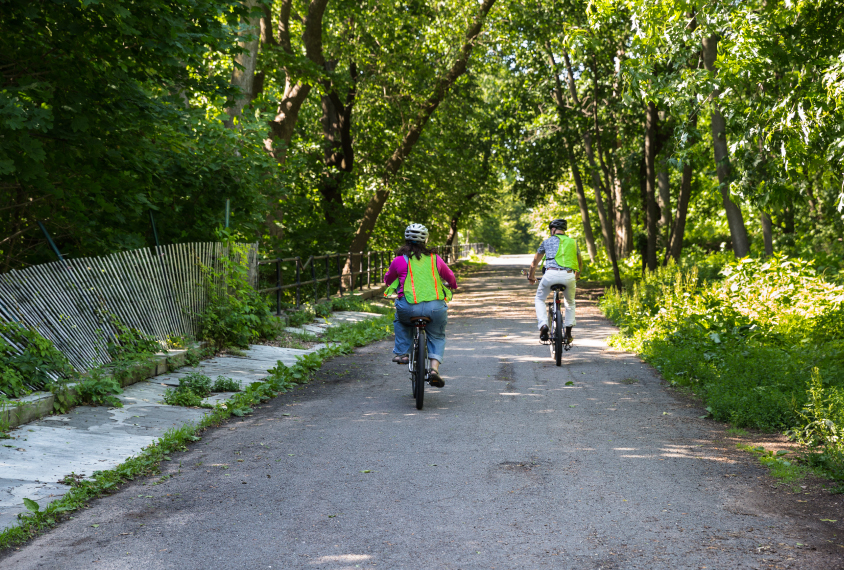 Photo: Gina and Bernardo ride bikes together, both wearing neon green visibility vests.