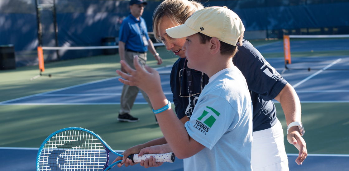 Boy holds tennis racket on court with teacher