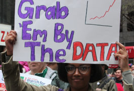 Woman at a protest holds a sign that says "Grab 'em by the data"