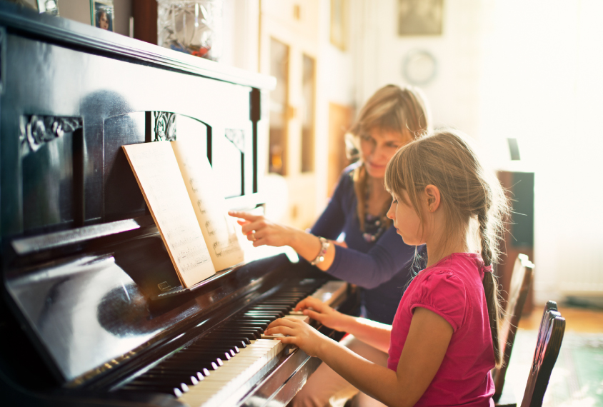 Girl playing the piano while a teacher guides her along the music.