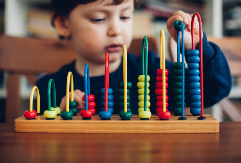 Toddler playing with stacking colorful beads on a toy.