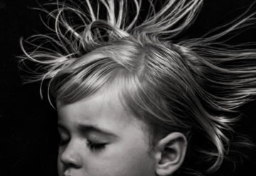 Toddler girl sleeping with hair floating against black background.