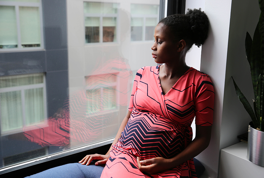 Pregnang woman sitting by window looking sad.