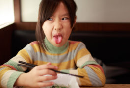 child sticking tongue out and making a face while holding chopsticks