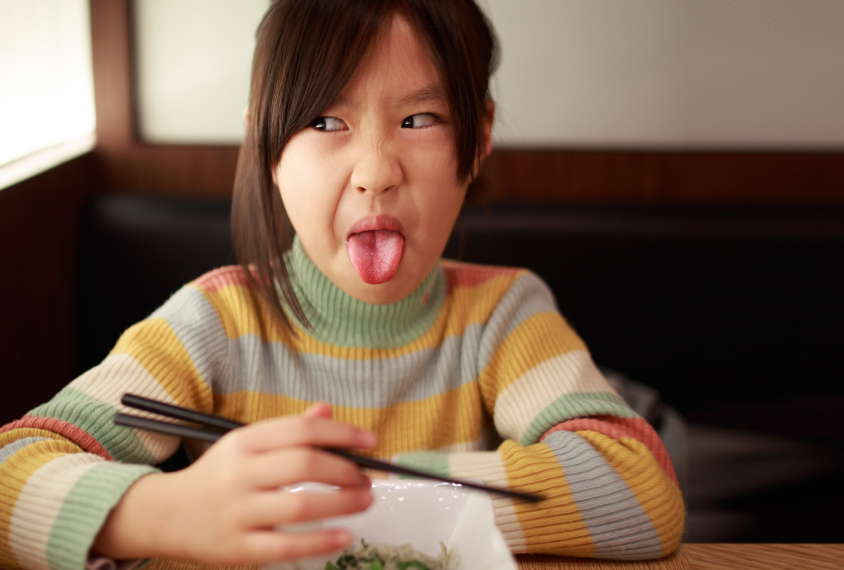 child sticking tongue out and making a face while holding chopsticks