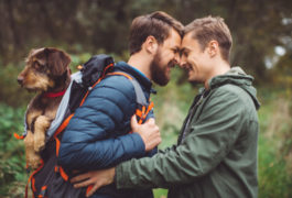two men hiking and embracing with dog in backpack