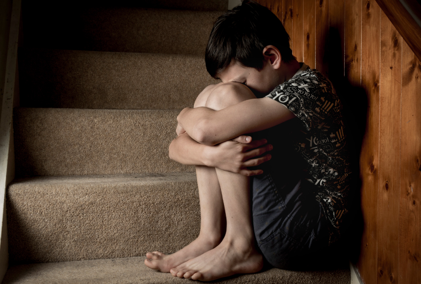 child anxiously sitting in stairwell holding knees closely