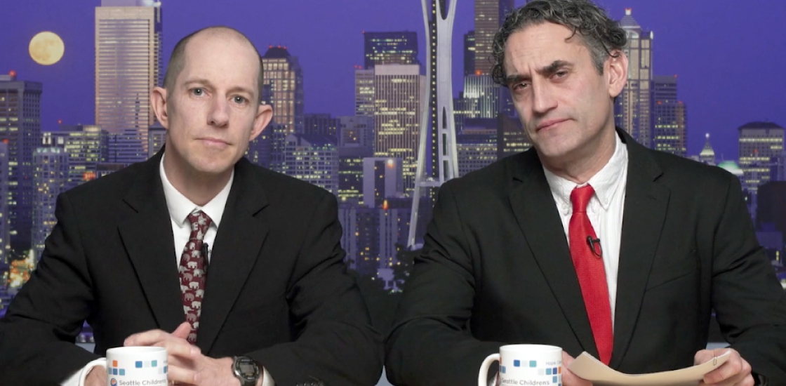 Two men dressed as news anchors look at the camera.