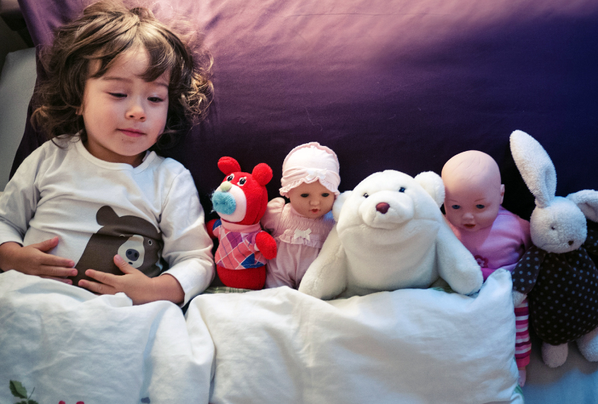 young girl sleeping with stuffed animals and dolls