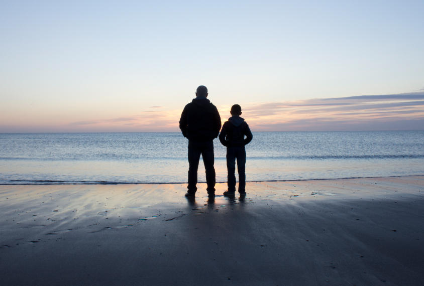 father and son standing on the beach during sunset