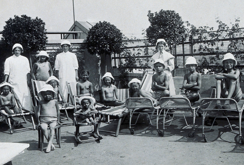 Vienna children's hospital, children in sun hats with attendants outdoors on chaise lounges and chairs.